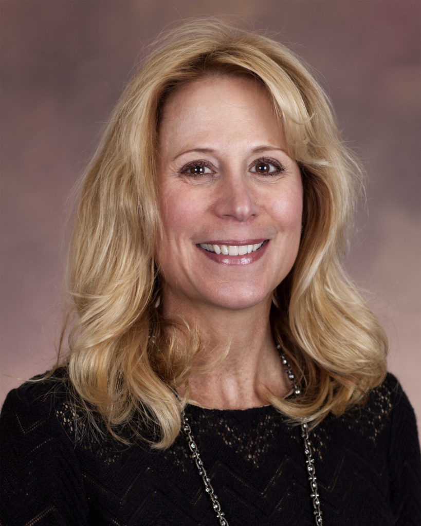 Susan Piergallini, a light-skinned woman with blonde hair wearing a black blouse, smiles