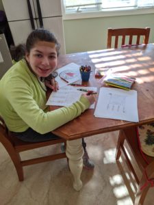 a young girl sits at a wooden table and colors pictures