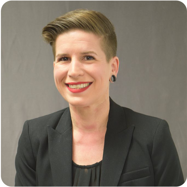 Kellie Goldberg, a light-skinned blonde woman with short blonde hair and wearing a black suit, smiles